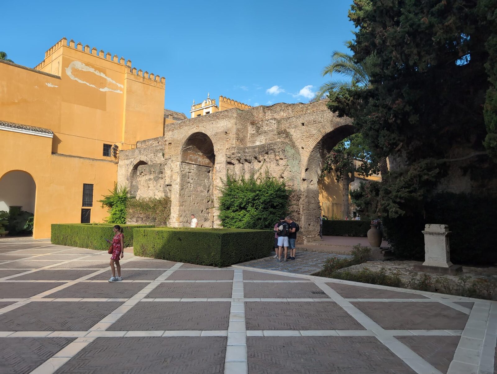 Stone arches, yellow walls, and clipped hedges in an Alcázar courtyard