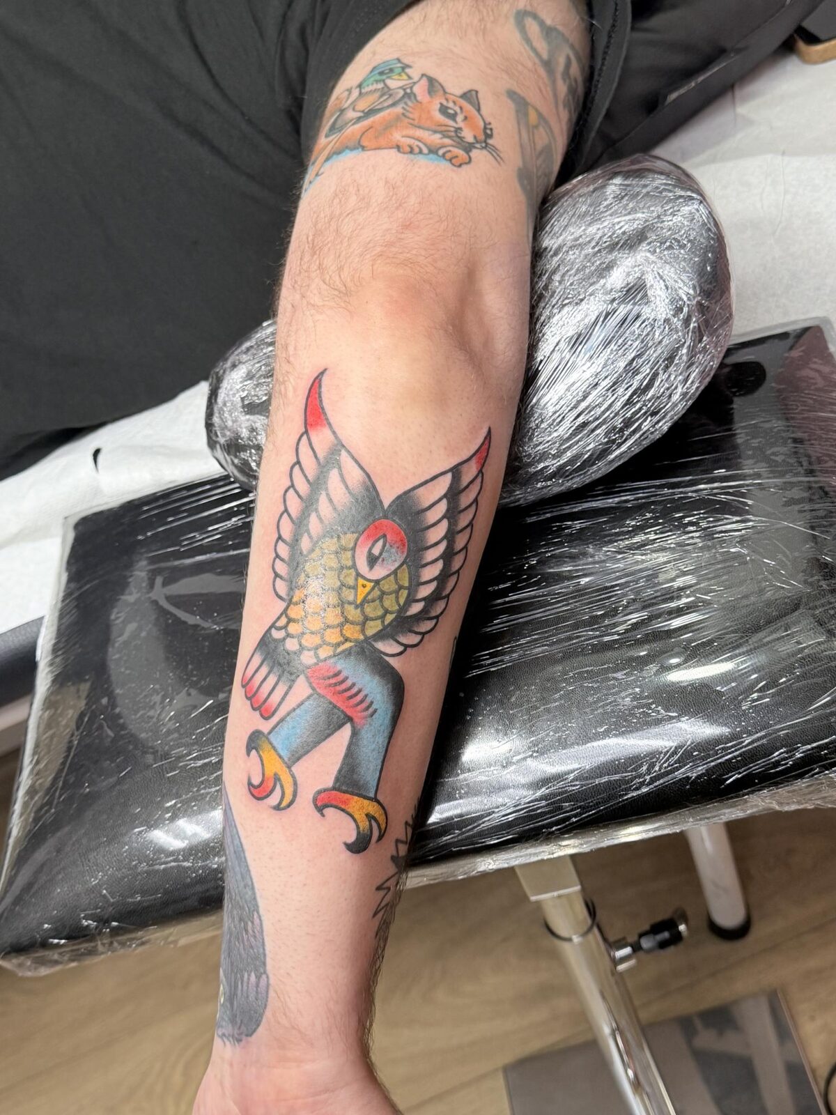 The fresh birdman tattoo by Javi Juelle at Lucero Tattoo, with raised wings, yellow scales, and red accents